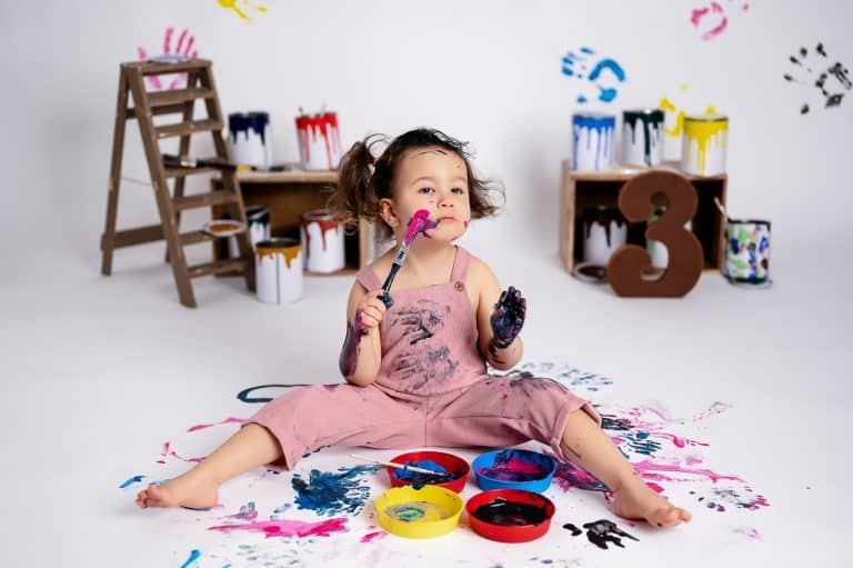 Little girl with paint on her hands and face during a Paint Party theme photoshoot