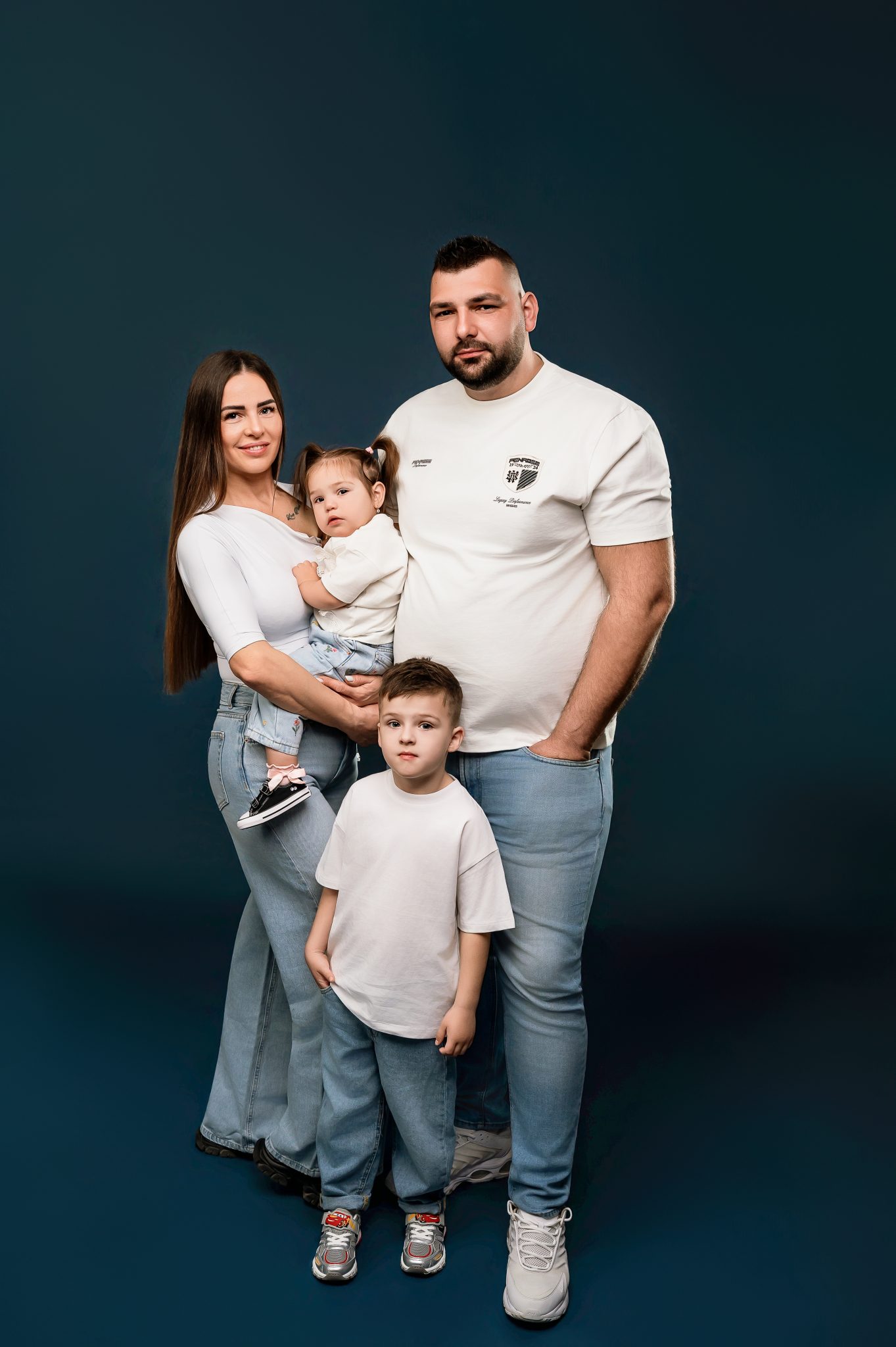 Happy family portrait with parents and two young children smiling at camera against teal background