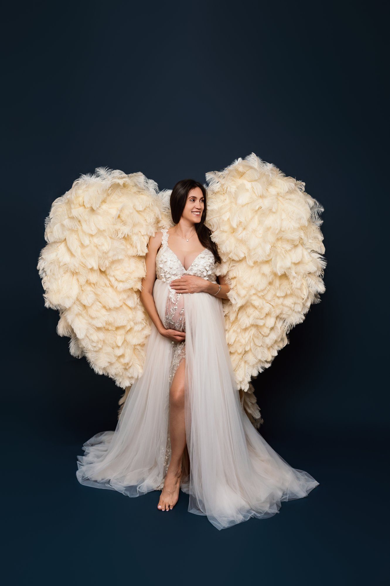 Pregnant woman in elegant red mermaid gown with flowing train posing with flowers