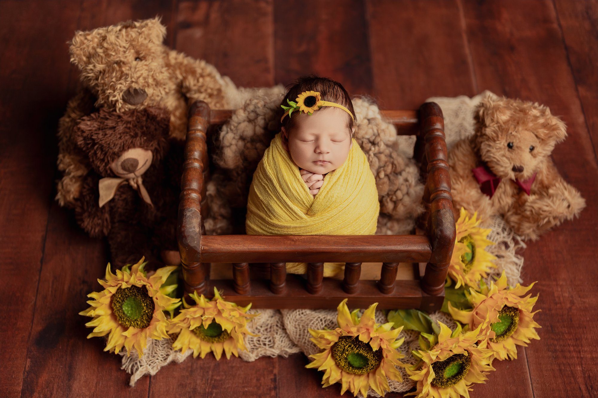 Newborn baby wrapped in yellow swaddle surrounded by teddy bears and sunflowers in Milton Keynes photo studio