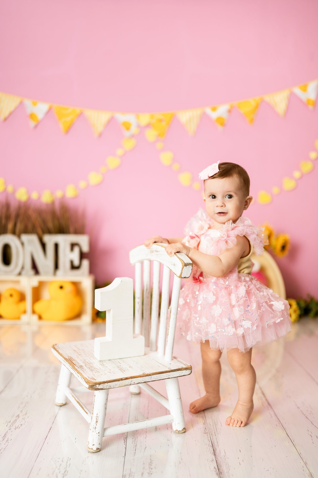 One year old girl in pink tutu smiling while playing with cake decorated with black ribbon at professional photography studio