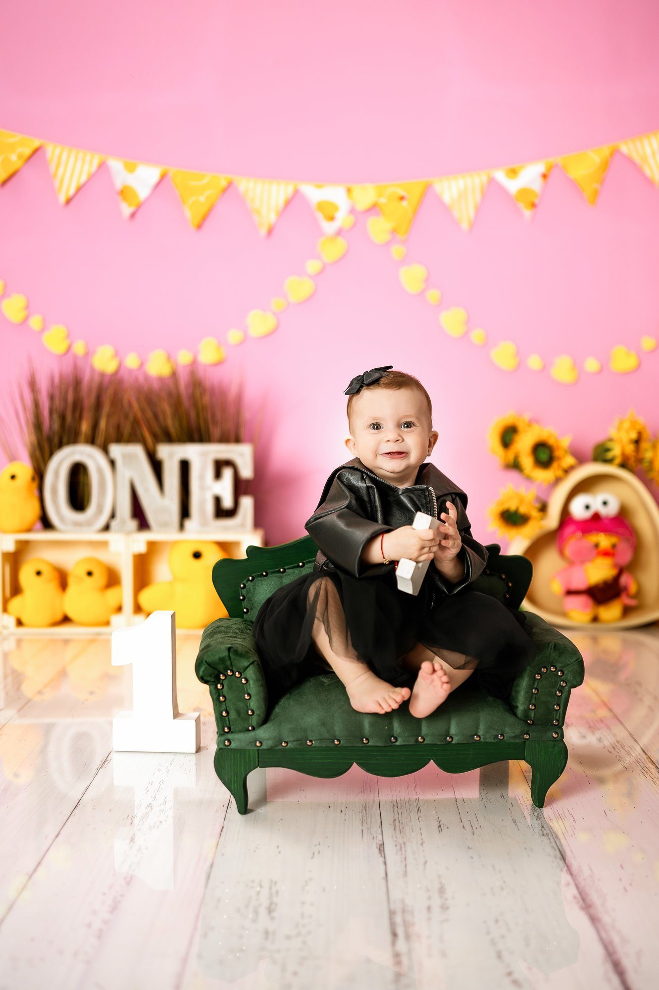 Toddler girl in pink dress posing with chair and number one prop during first birthday cake smash photography