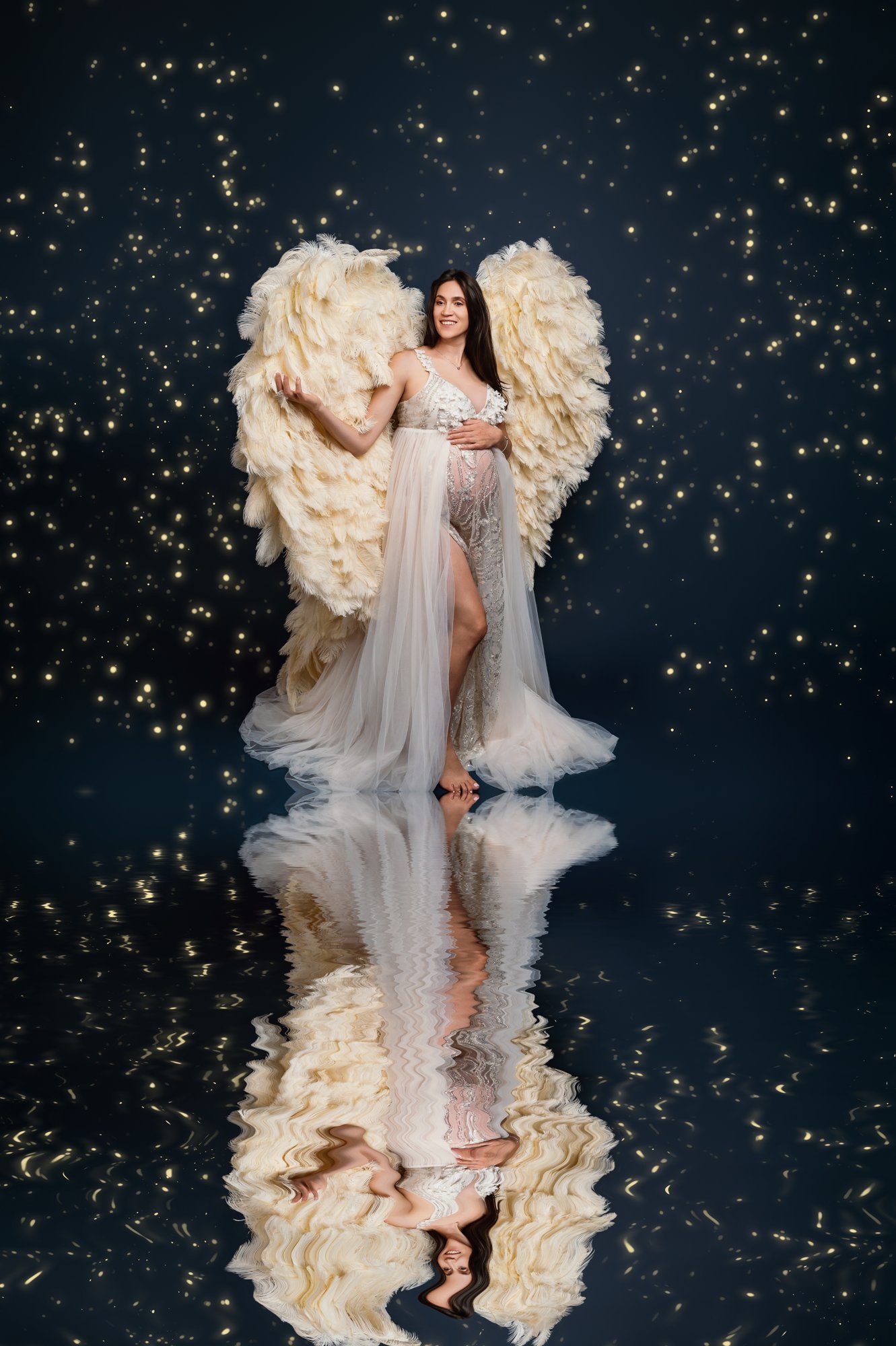 Maternity portrait with angelic feathered wings against dark background with golden lights
