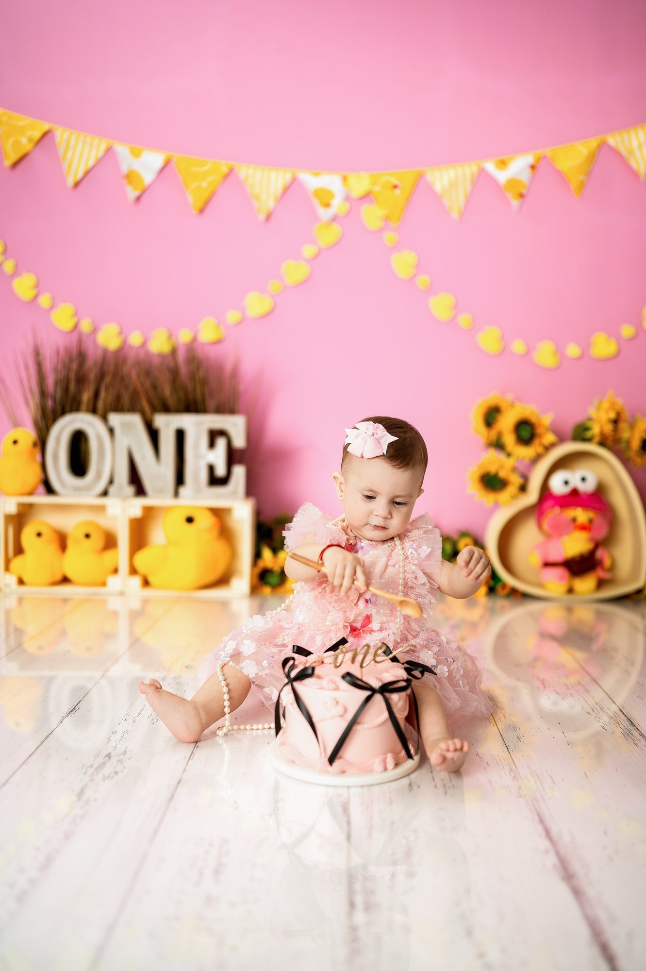 Little girl with white hair bow posing during first birthday cake smash photo session