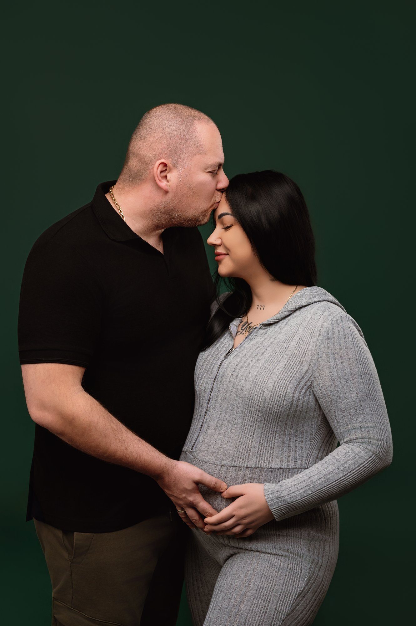 Pregnant woman cradling bump in red dress against green background for maternity photography