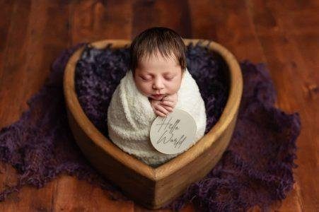 Newborn wrapped in purple in a heart-shaped basket