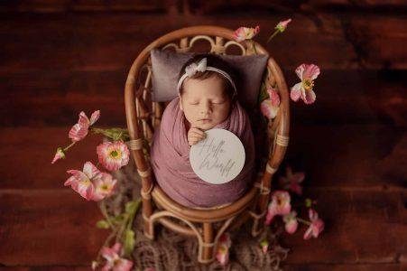 Newborn wrapped in dusty pink on a cane chair with flowers