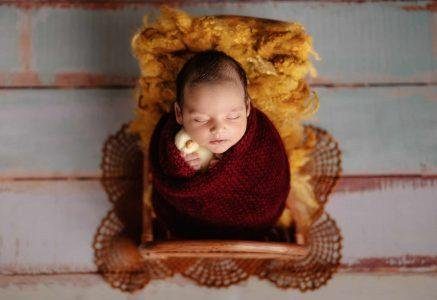 Newborn wrapped in mustard gold in a whitewashed basket