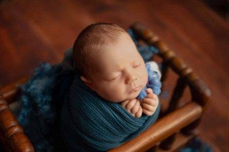 Newborn wrapped in teal blue on a wooden chair