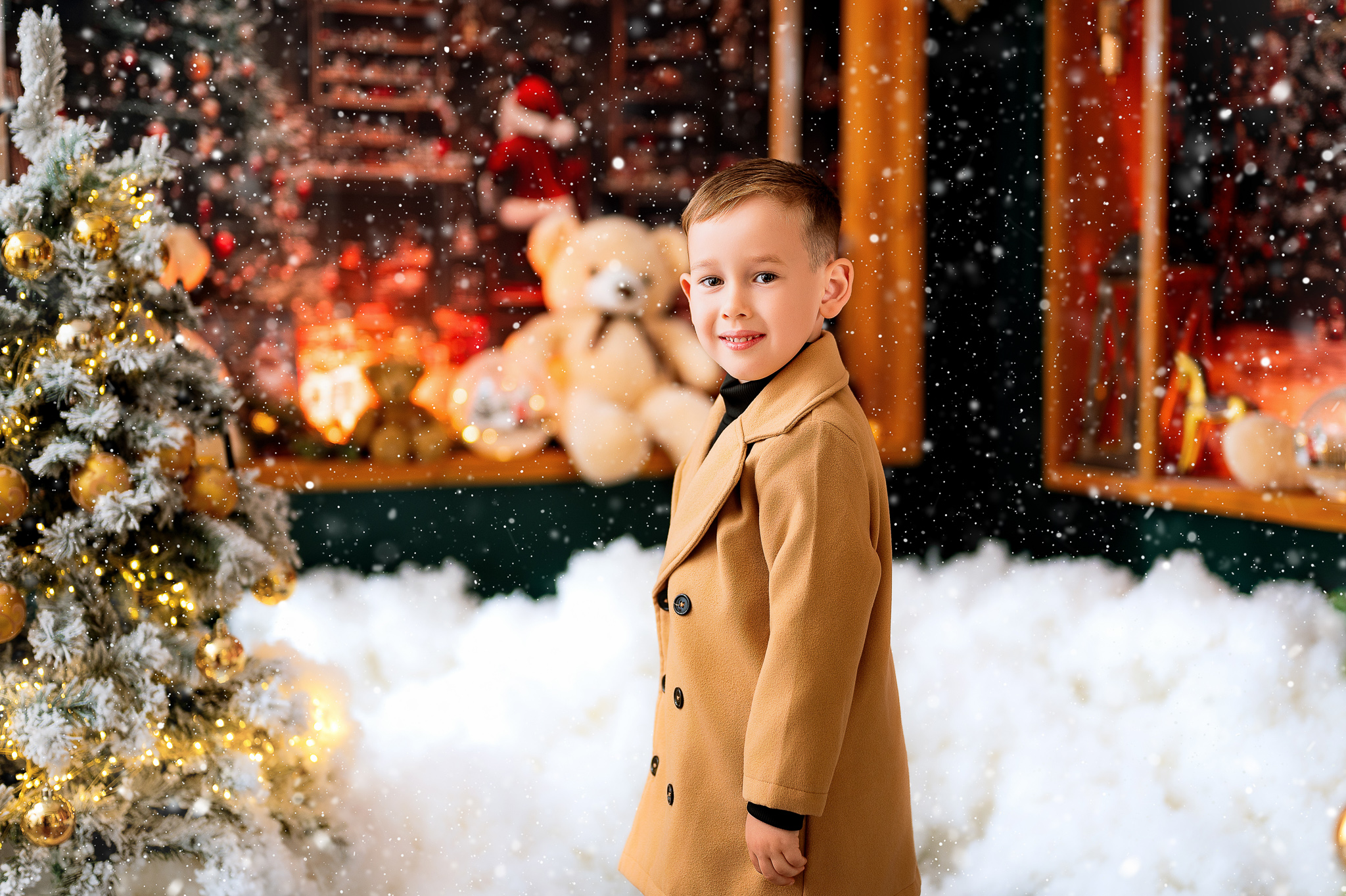 Little boy in a camel coat in the snowy Santa's workshop set, a real session from Christmas 2025