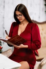 Woman in a red velvet dress reading a book at a white desk, Christmas photoshoot