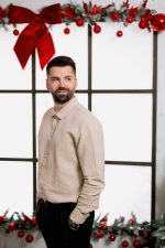 Man in a beige jumper beside a studio window with Christmas garlands