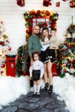 Family of four beside a red door and postbox in the snow, Christmas photoshoot