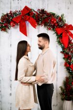 Couple holding each other under a red bow garland, Christmas photoshoot Northampton