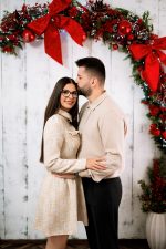 Couple embracing under a red bow garland on white panelling, Christmas couple photoshoot