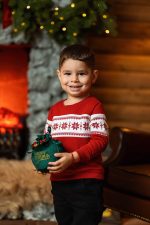 boy in red Christmas jumper holding Christmas gift by fireplace Milton Keynes