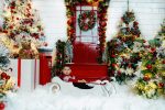 baby in white onesie lying in white sleigh by red Christmas door Northampton