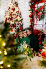 family of three in matching burgundy Christmas pyjamas by decorated Christmas tree Northampton