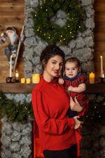 mother in red jumper holding baby in red tartan outfit by fireplace Christmas Northampton
