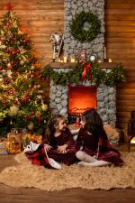 two sisters in matching burgundy velvet dresses sitting by stone fireplace Northampton