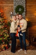 family of four parents and two daughters in Christmas jumpers by red festive door Northampton