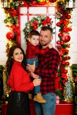 family of three in matching cream Christmas jumpers sitting by stone fireplace Northampton