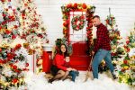 family of three parents and toddler boy standing by red Christmas door in fake snow Northampton