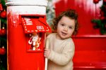 toddler girl in cream sweater next to red Santa mailbox Christmas photoshoot Northampton